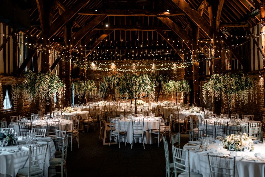 The Tithe Barn set for a wedding breakfast beneath exposed beams and strings of lights